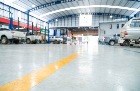A spacious, modern automotive service garage featuring multiple vehicle bays with various cars undergoing mechanical repairs and maintenance lifts.