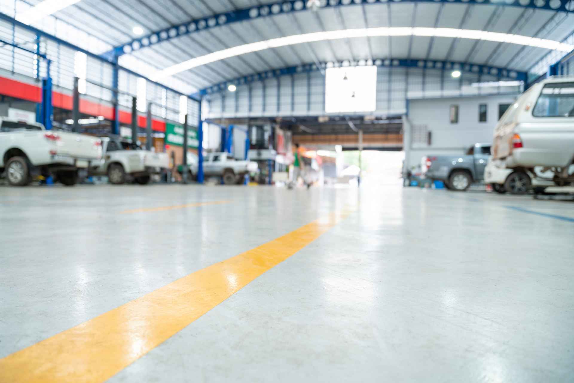 A spacious, modern automotive service garage featuring multiple vehicle bays with various cars undergoing mechanical repairs and maintenance lifts.